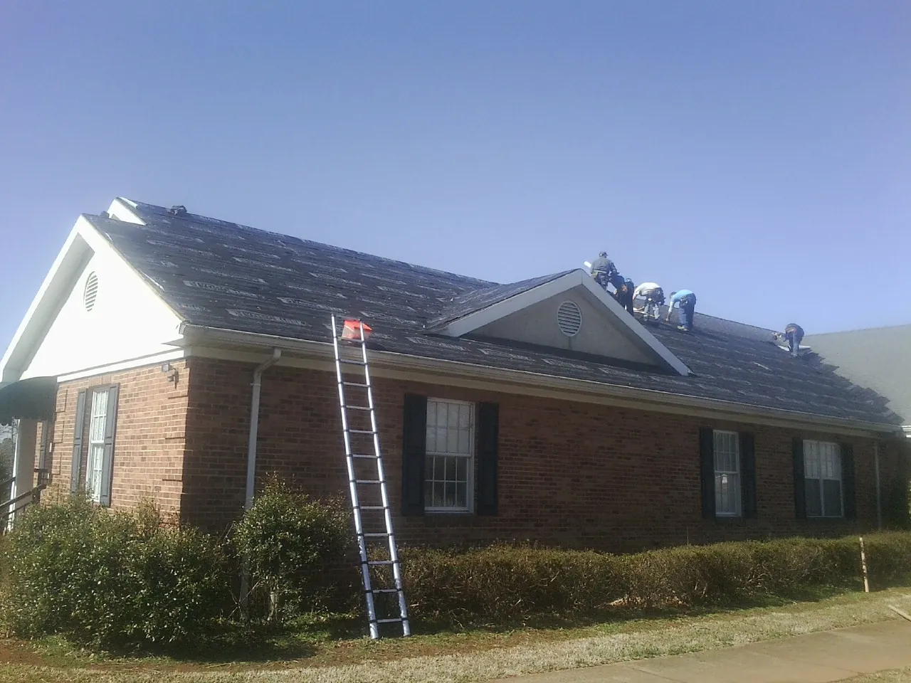 Crew tearing shingles off a brick ranch roof with a ladder set — Emergency Roof Repair work by our crew in Dysart