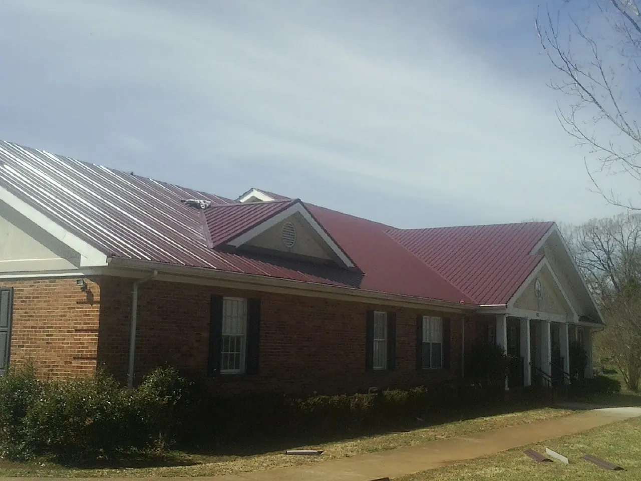 Red metal roof with gabled entries on a long brick building, from a Hail Damage Roof Repair job in Dysart