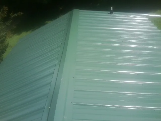 New green metal panels meeting at the ridge of a roof — Flat Roof Repair work by our crew in Dysart