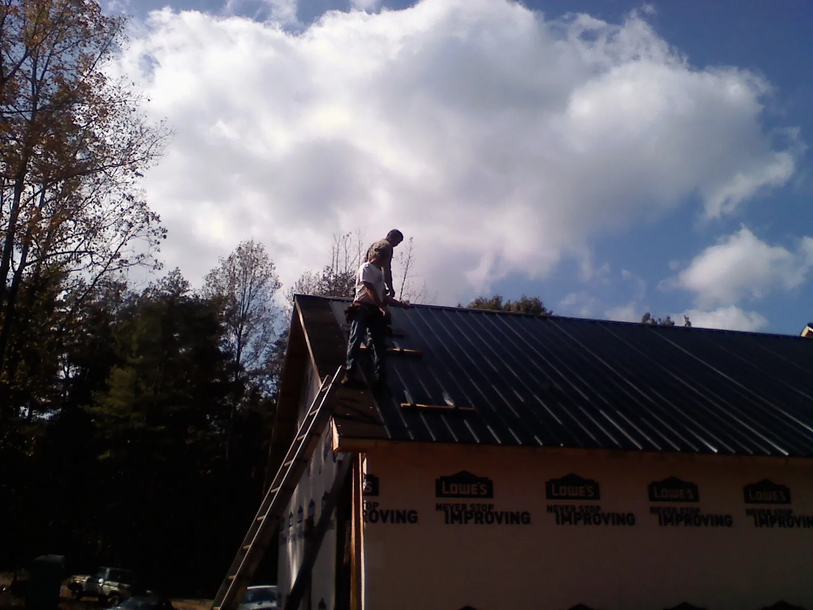 Roofer fastening dark metal panels high against a cloudy sky, from a Roof Inspection job in Dysart