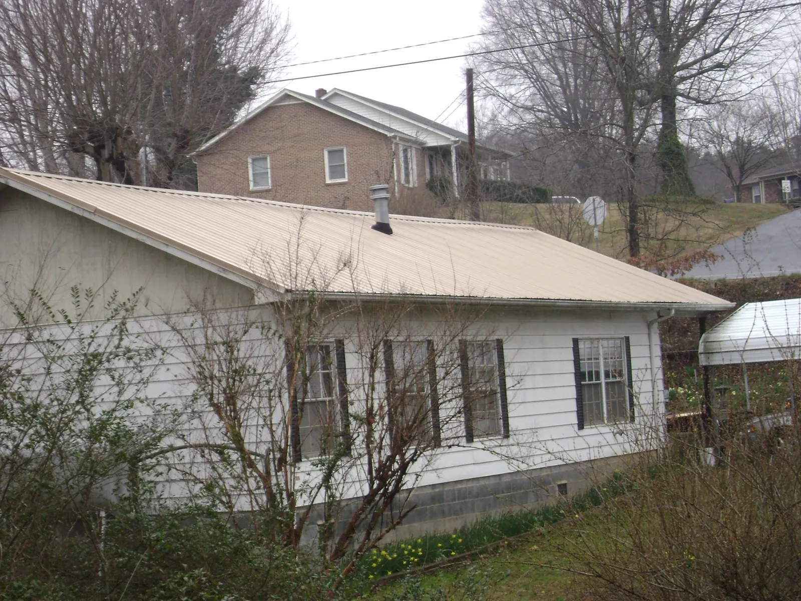 Tan metal roof on a white sided house set into a hillside — Commercial Roofing by Roofing Brothers in Dysart