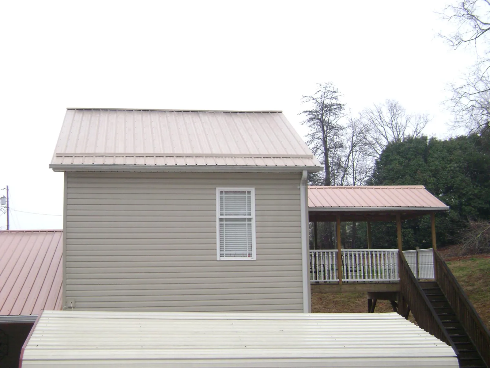 Tan metal roofs on a two story addition and attached porch, from a Roof Replacement job in Dysart